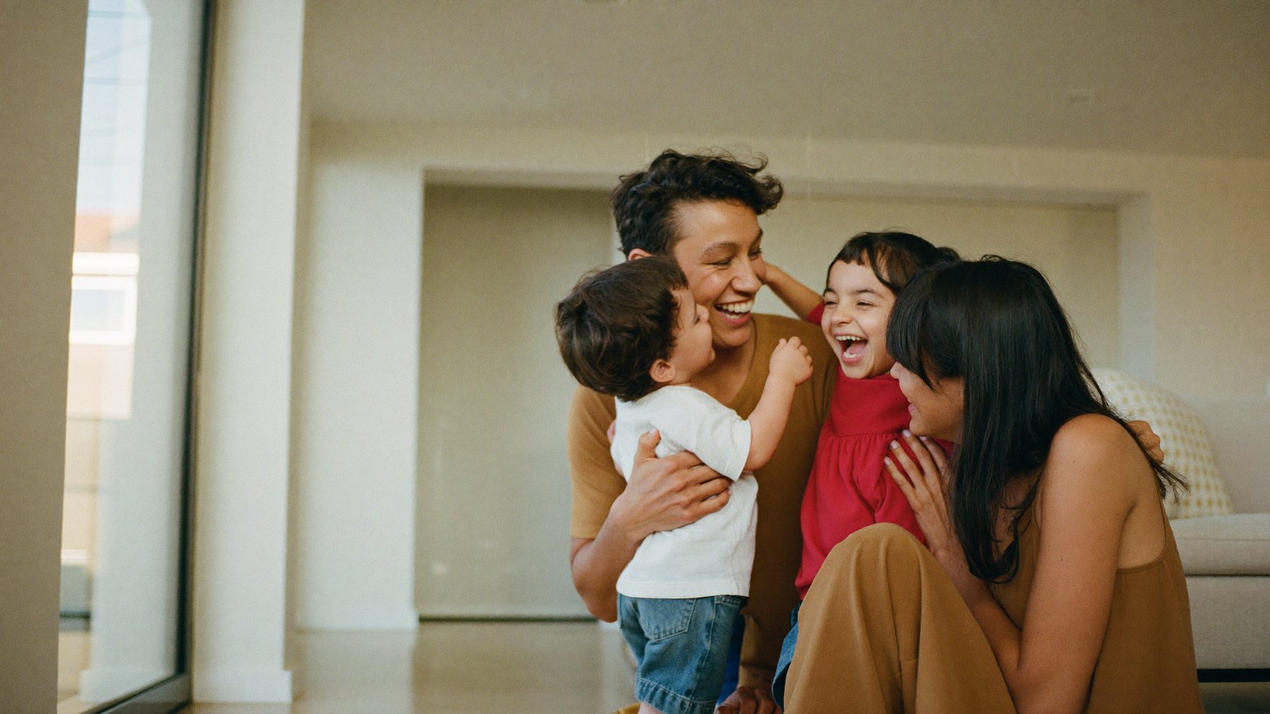 Pareja joven hispana riendo en casa con sus dos hijos pequeños